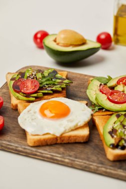 kesme tahtası tost, çırpılmış yumurta, domates ve gri arka plan üzerinde avokado ile seçici odak