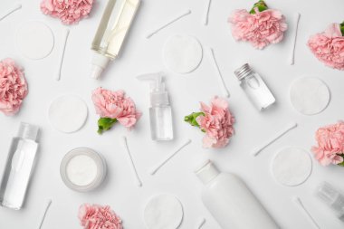 Top view of different cosmetic bottles, carnations flowers, cotton sticks and cosmetic pads on white background clipart