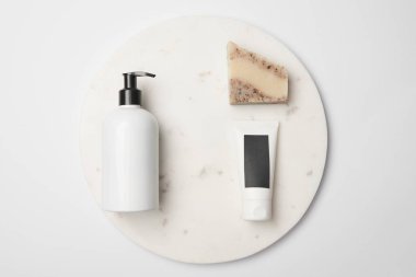 Top view of different cosmetic bottle, tube and soap on white round surface
