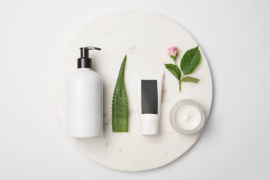 Beyaz yuvarlak yüzey üzerinde farklı kozmetik kapları, aloe vera yaprağı ve gül çiçek üstten görünüm