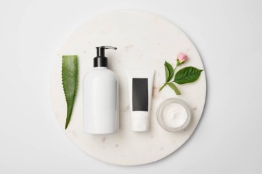 Beyaz yuvarlak yüzey üzerinde farklı kozmetik kapları, aloe vera yaprağı ve gül çiçek üstten görünüm