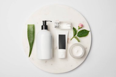 Beyaz yuvarlak yüzey üzerinde farklı kozmetik kapları, aloe vera yaprağı ve gül çiçek üstten görünüm