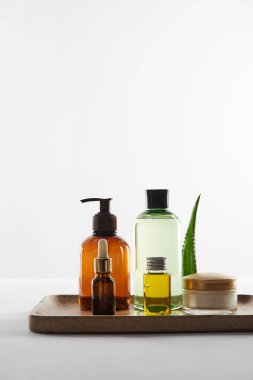 Çeşitli kozmetik kapları ve aloe vera yaprak beyaz arka plan üzerinde ahşap tepsi