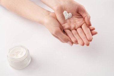 Partial view of woman applying cosmetic cream in heart shape on white background clipart