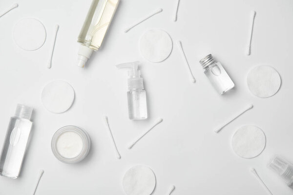 Вид сверху на различные косметические бутылки, хлопковые палочки и косметические подушечки на белом фоне
