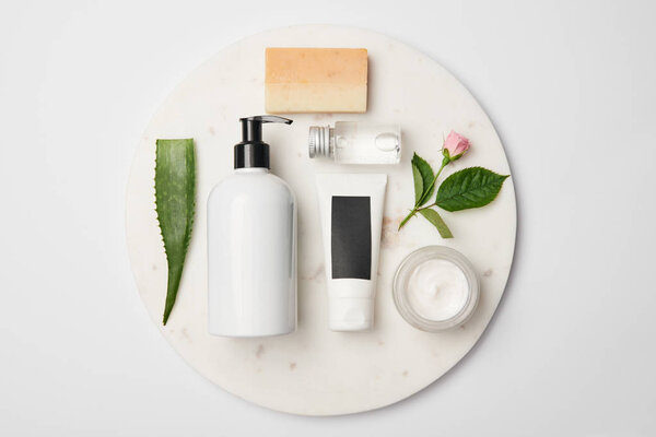 Top view of different cosmetic containers, soap, aloe vera leaf and rose flower on white round surface