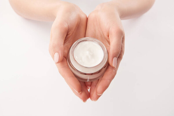Partial view of woman applying cosmetic cream on white background