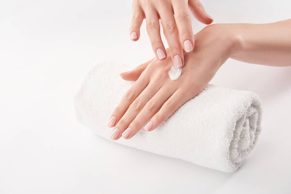 Partial view of woman applying cosmetic cream on white background