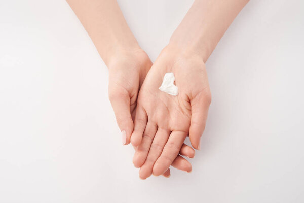 Partial view of woman applying cosmetic cream in heart shape on white background