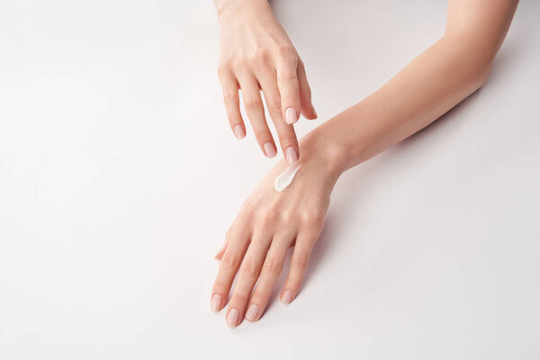 Partial view of woman applying cosmetic cream on white background