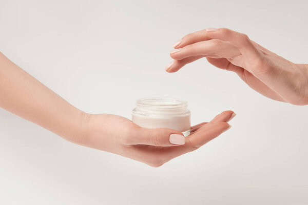 Partial view of woman applying cosmetic cream on white background