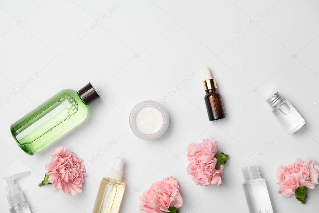 Top view of different cosmetic containers and pink carnations flowers on white background