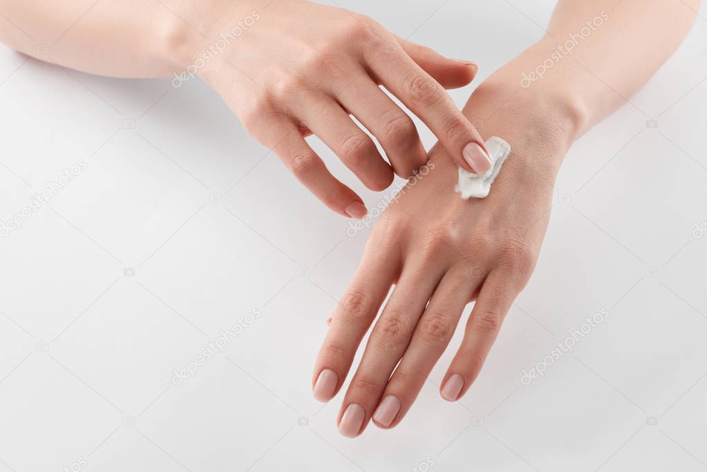 Partial view of woman applying cosmetic cream on hands on white background 