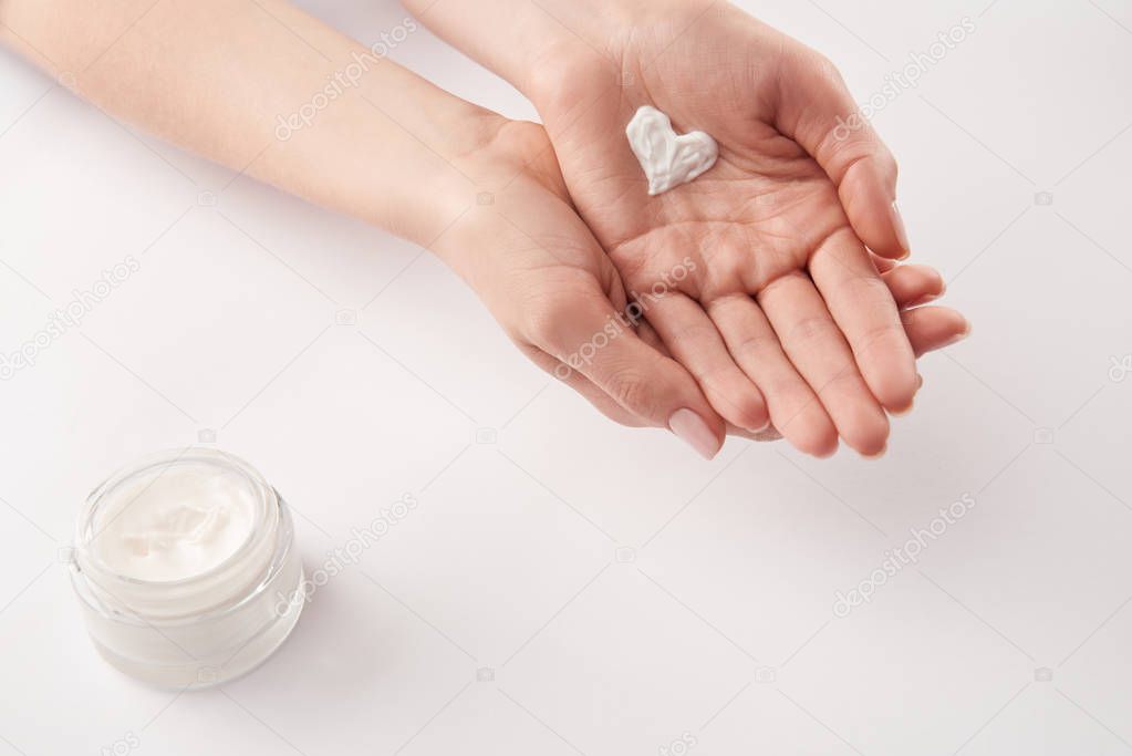 Partial view of woman applying cosmetic cream in heart shape on white background