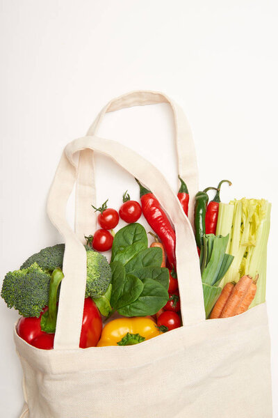 Studio shot of spinach leaves and vegetables in eco bag on white background