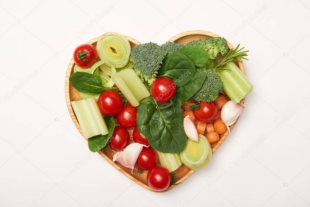Top view of vegetables on heart shaped cutting board on white background