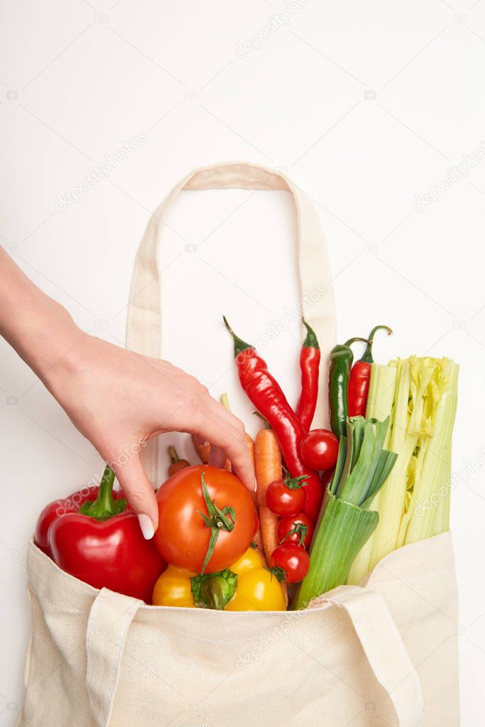 Partial view of woman taking out tomato of bag with vegetables on white background