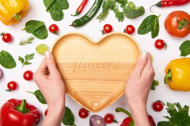 Partial view of woman holding wooden cutting board and vegetables on white background clipart