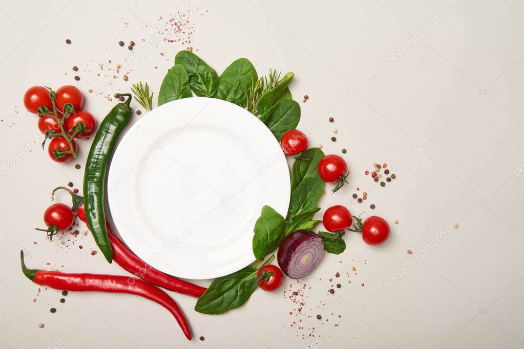 Top view of white plate, vegetables and spices on grey background