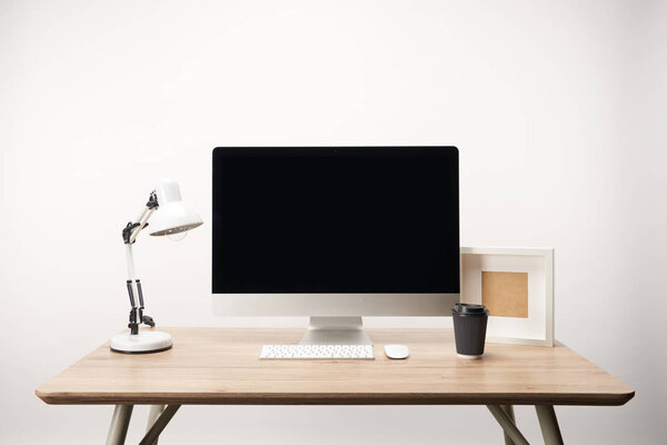 workplace with lamp, coffee to go, photo frame and desktop computer with copy space isolated on white