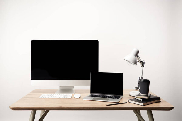 workplace with lamp, coffee to go, notebooks, desktop computer and laptop with copy space isolated on white