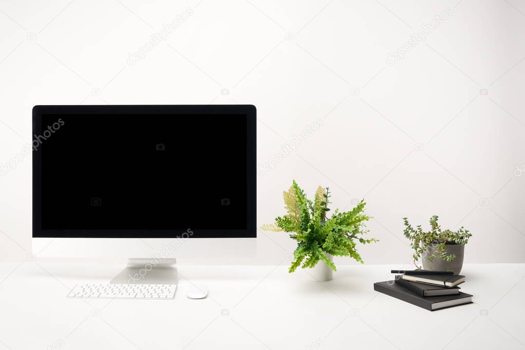 workplace with green plants, notebooks and desktop computer with copy space isolated on white