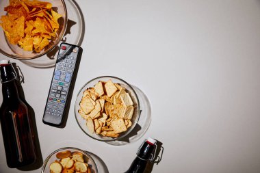 Beyaz arka plan üzerinde uzaktan kumanda ve aperatifler yakınındaki şişe üstten görünüm