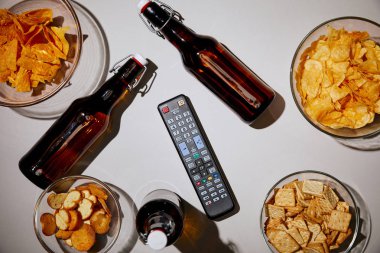 Beyaz arka plan üzerinde kahverengi şişe bira yakınındaki aperatifler kase ve uzaktan kumanda ile üstten görünüm