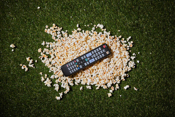 top view of popcorn lying near remote control on green grass