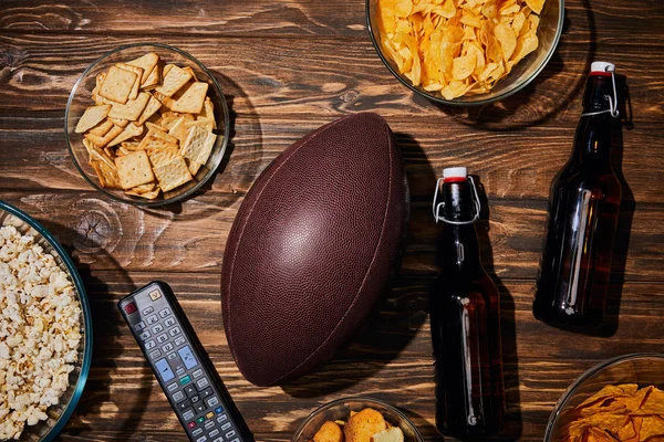 top view of party snacks in bowls near brown bottles with beer and ball on wooden table