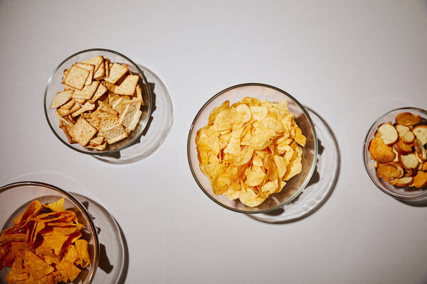 top view of glass bowls with tasty snacks on white background