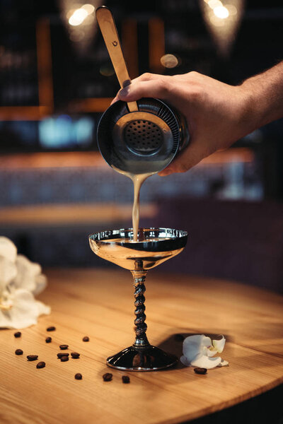 selective focus of bartender pouring cocktail from shaker through sieve in metal glass 