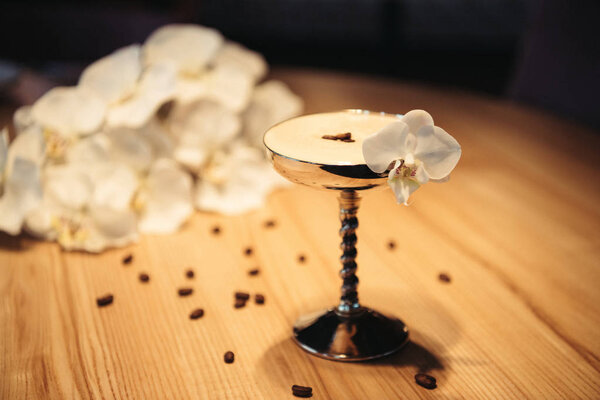 selective focus of alcoholic cocktail in metal glass decorated with orchid flower on wooden table