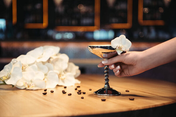 cropped view of woman holding alcoholic cocktail in metal glass decorated with orchid flower and coffee beans
