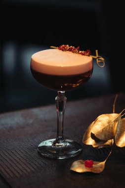 selective focus of alcoholic cocktail with foam and dry flowers on dark background clipart