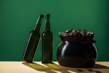 beer bottles and black pot with golden coins isolated on green, st patrick day concept clipart