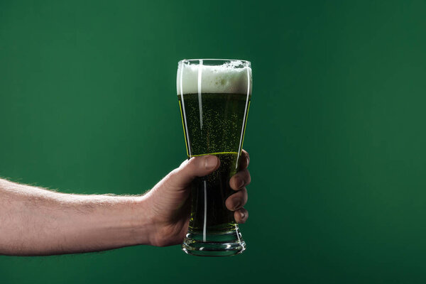 обрезанный вид человека, держащего бокалы пива с пеной, изолированной на зеленой концепции дня Святого Патрика
