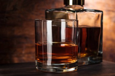close-up view of glass of whiskey and bottle on wooden table  clipart