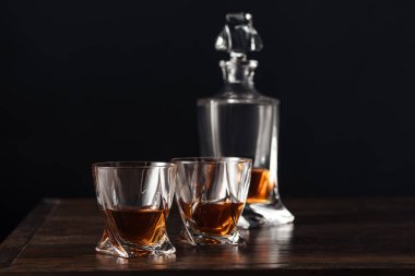 close-up view of glasses and bottle of whisky on dark wooden table isolated on black   clipart