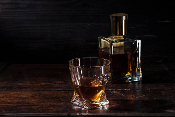 коньяк в стекле и бутылка роскошного алкоголя на темном деревянном столе
