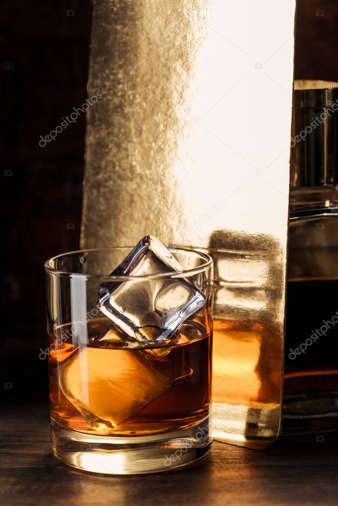close-up view of glass of amber alcohol with ice cubes on wooden table