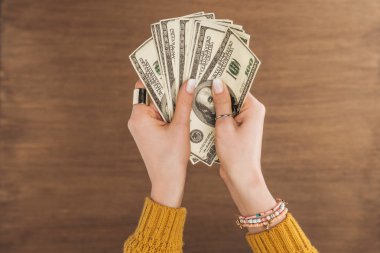 top view of woman holding dollars banknotes on wooden background clipart