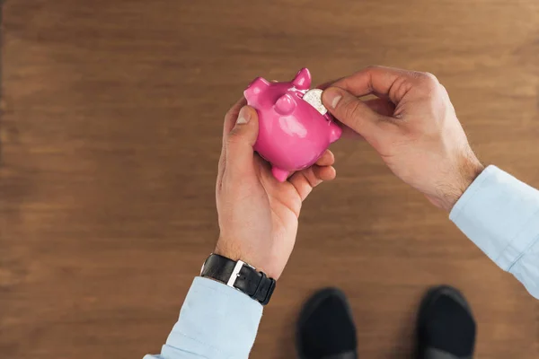 Vista Superior Homem Colocando Rosa Piggy Banco Moeda Fundo Madeira — Fotografia de Stock