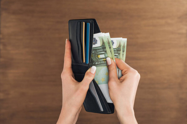 top view of woman puting euros banknotes in wallet on wooden background