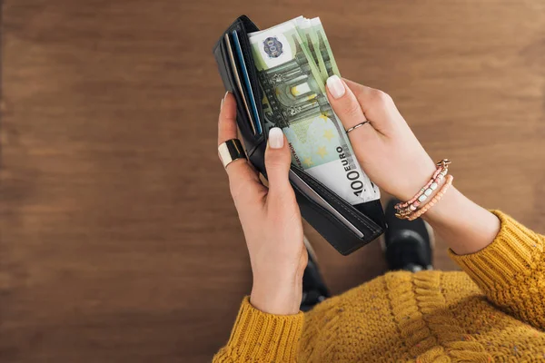 妇女从钱包里拿欧元钞票的顶部视图在木制背景 — 图库照片