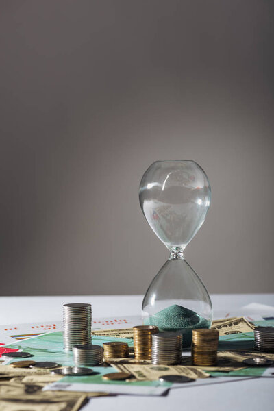 hourglass and coins stacks on different banknotes with grey background