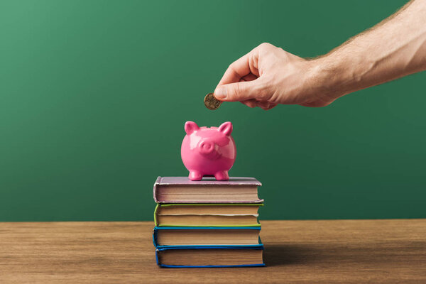 man puting coin in piggy bank on books and green background