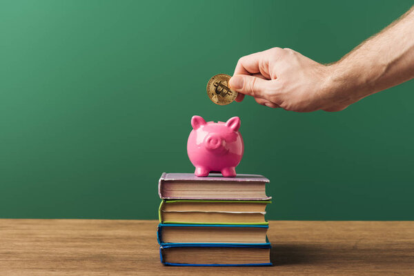 man puting coin in pink piggy bank on books with green background