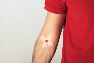Partial view of patient in red t-shirt with plasters on grey background, blood donation concept clipart