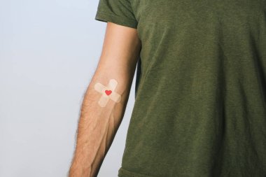 Partial view of patient in green t-shirt with plasters on grey background, blood donation concept clipart